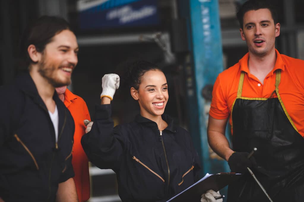 Group of car mechanics wearing uniform with cap and gloves in garage celebrating